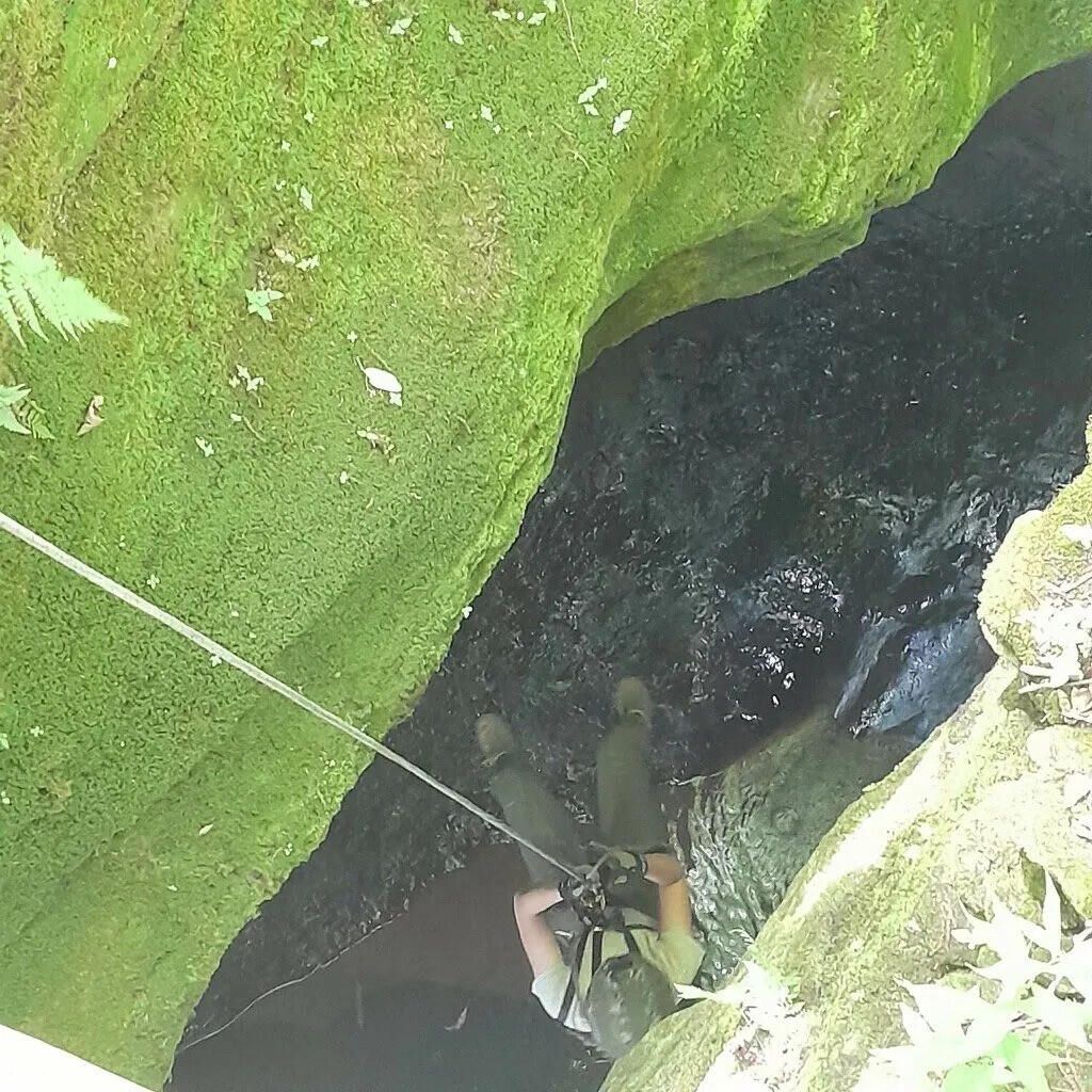Looking down a mossy rock crevice at a rescuer on rope
