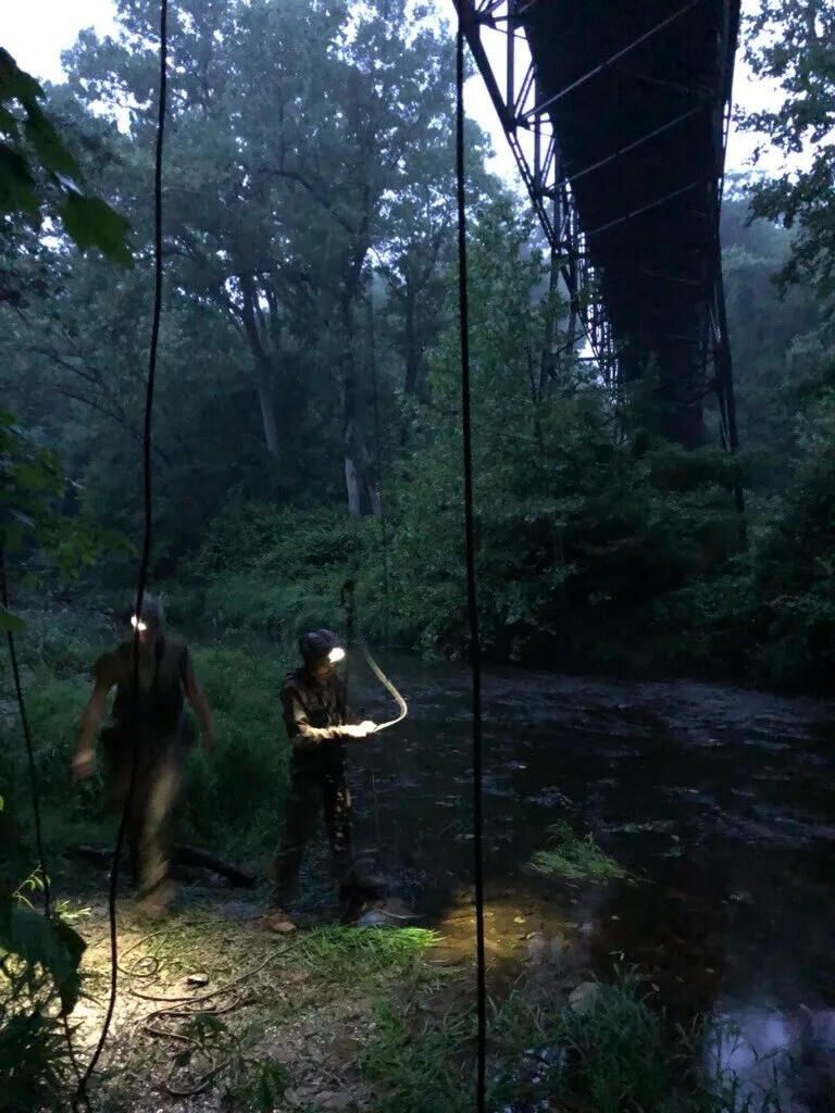Two people on ropes under a bridge at dusk, headlamps on